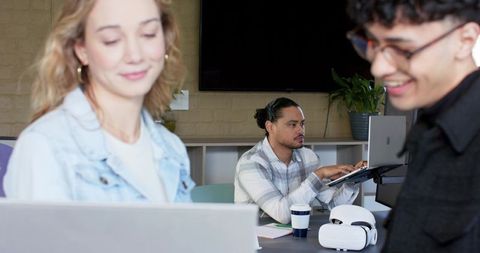 Diverse team collaborating at meeting table using laptop and vr headset