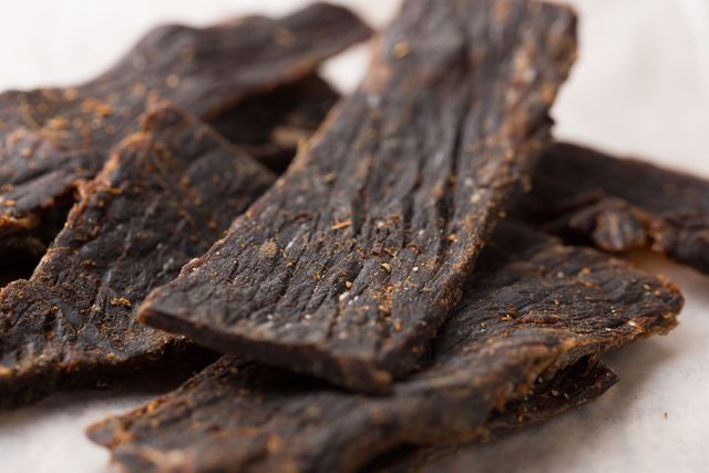This close-up shows several slices of crispy beef jerky on a white background. Ideal for use in food blogs, protein snack advertisements, and healthy eating promotions. Also great for articles on high-protein foods or recipes using beef jerky.