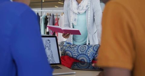 Fashion designer consulting clients with sketchbook, tape measure and fabric samples in boutique