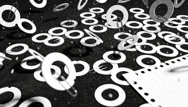 Scattering white paper reinforcement rings and metal clips on dark desk surface