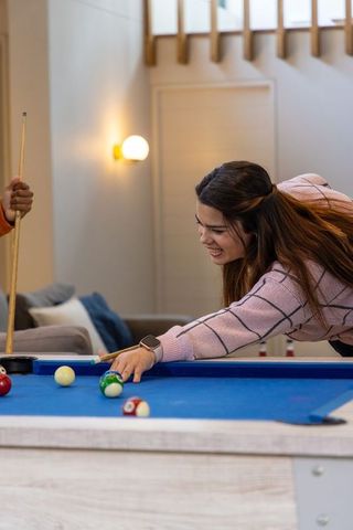 Asian woman playing pool with friend in cozy loft living room wearing smartwatch