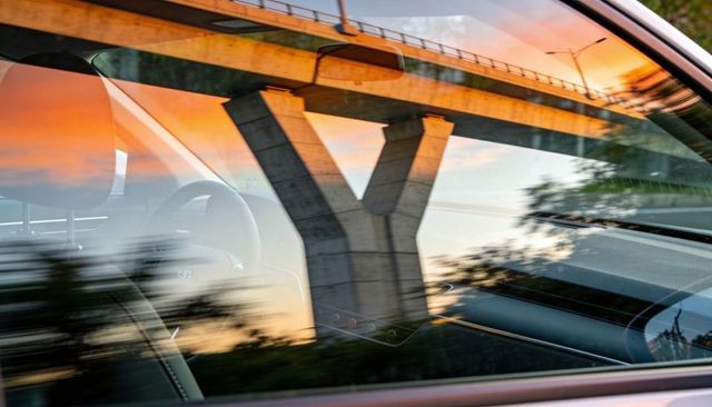 Car interior reflecting y-shaped overpass at sunset, steering wheel and headrest visible