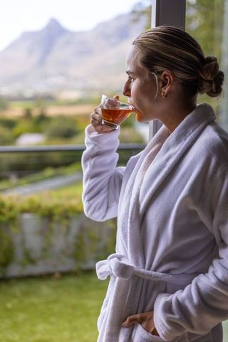 Morning relaxation on balcony drinking tea in white robe with scenic mountain view