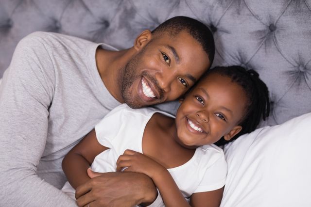 Father and daughter lying on bed at home, smiling and enjoying a moment of bonding. Perfect for use in family-oriented advertisements, parenting blogs, and articles about father-daughter relationships. Ideal for promoting family values, happiness, and togetherness.