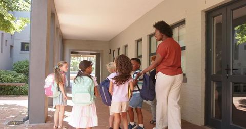 Diverse schoolchildren and teacher gathering at school entrance with backpacks
