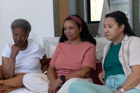 Three african american women sitting reflecting on sofa in bright minimal living room