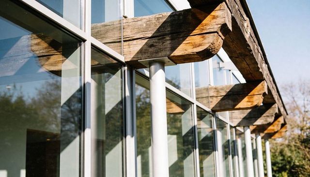 Weathered timber beams casting graphic shadows across modern glass facade