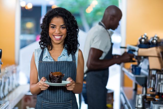 Portrait of smiling waitress holding a plate of cupcake in cafÃ©