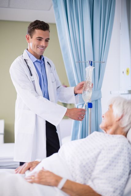 Doctor adjusting IV drip for elderly patient lying in hospital bed. Ideal for use in healthcare, medical care, patient treatment, and hospital-related content. Can be used in articles, brochures, and websites focusing on healthcare services, patient care, and medical treatments.
