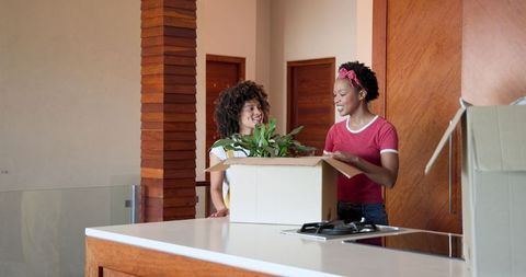 Lesbian couple unpacking boxes and arranging plants in new home