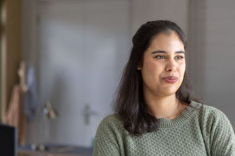 Contemplative young woman looking away in cozy olive sweater indoor natural light portrait