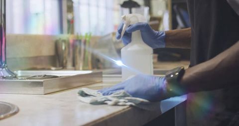 Cleaning marble countertop with spray bottle and microfiber cloth, gloved hands close-up