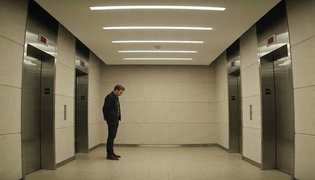 Solitary man waiting in minimalist modern office elevator lobby with stainless steel doors