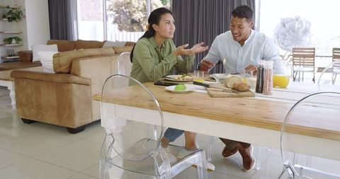 Asian woman and partner sharing casual breakfast and conversation at modern open-plan dining table