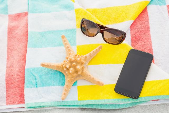 Close -up of starfish, sunglasses and mobile phone kept on beach blanket at beach