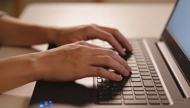 Typing hands on laptop keyboard in home workspace with soft ambient light