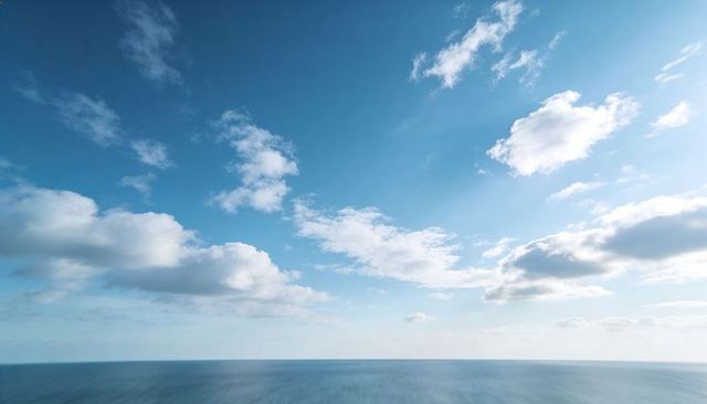 Calm ocean stretching to horizon under blue sky with scattered white clouds panoramic seascape