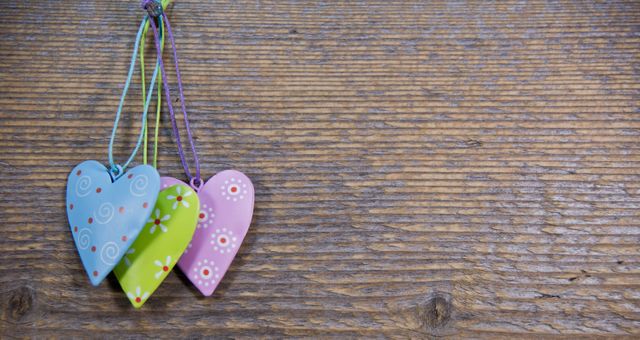 Three colorful wooden hearts with intricate patterns hang against a textured, rustic wooden surface. Use for Valentine’s Day themes, love, romance, crafty DIY projects, handmade or artisanal product promotions, and home decor inspiration.