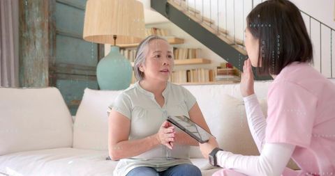 Senior woman consulting caregiver using tablet during home health visit