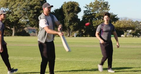 Friends playing cricket in park practicing batting and bowling with pink ball