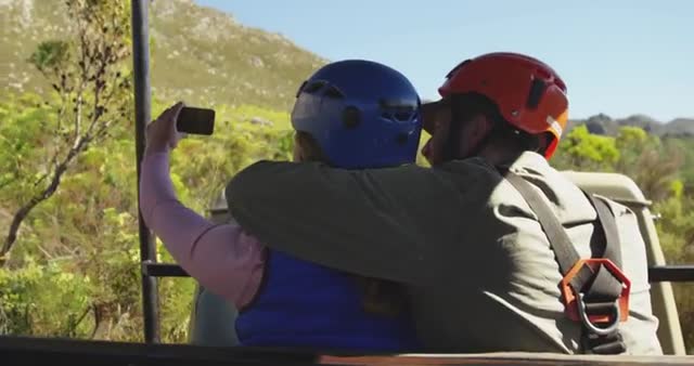 A young couple in zip lining gear enjoys an adventurous moment in the mountains, capturing memories with a selfie. Ideal for use in travel brochures, articles on adventure vacations, or advertisements promoting tourism in South Africa, highlighting outdoor activities.