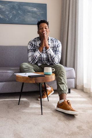 African american man sitting on gray sofa holding documents and phone in cozy living room