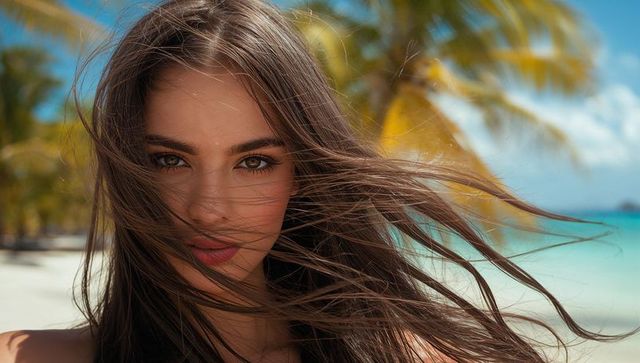 Sunlit brunette with windswept hair on tropical beach close-up portrait with palm trees