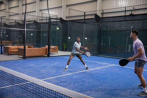 Diverse male teammates playing padel on blue indoor court in dynamic high-energy doubles action