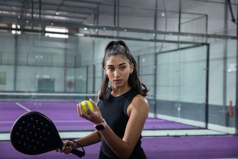 Tossing ball and serving on purple padel court featuring focused female player