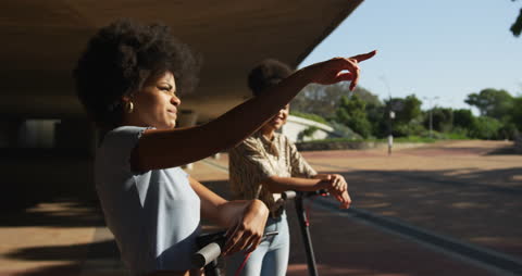 Friends Enjoying Ride on Scooters in Urban Park on Sunny Day