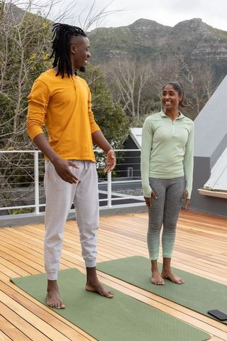 Diverse duo practicing rooftop yoga barefoot on green mats with mountain view