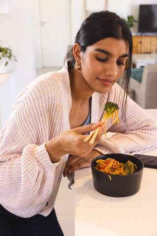 South asian woman enjoying noodles at home with chopsticks