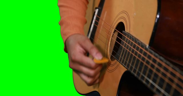 Close-up image of person strumming acoustic guitar, visible hand wearing orange sleeve. Green screen background for easy editing in videos or graphic projects. Useful for music tutorials, promotional materials, and creative multimedia presentations.