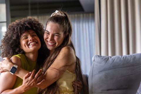 Sharing warmth hugging together: diverse female friends embracing on living room sofa