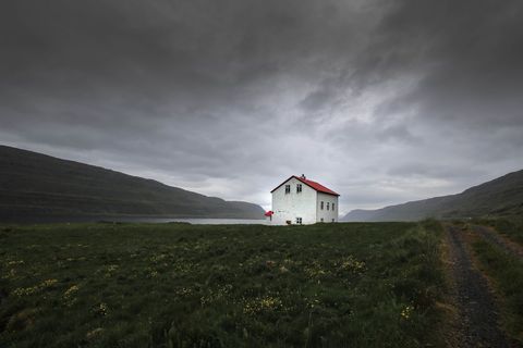 Solitary White House with Red Roof on Moody Fjord Meadow under Stormy Overcast Sky