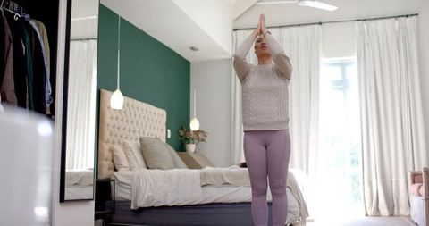 Woman practicing yoga in modern bedroom with green accent wall
