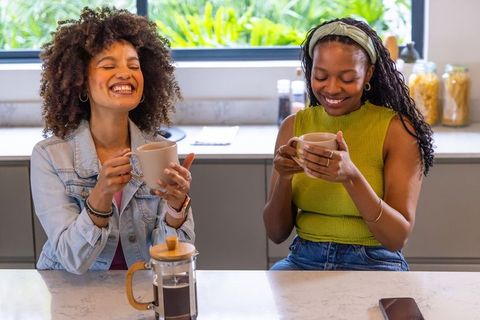 Two african american women laughing and enjoying coffee at kitchen island in morning light