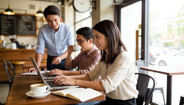 Young professionals collaborating in coffeehouse on laptops, remote work and teamwork