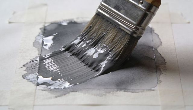 Brushing glossy charcoal wash on taped paper, macro detail of bristles and wet pigment