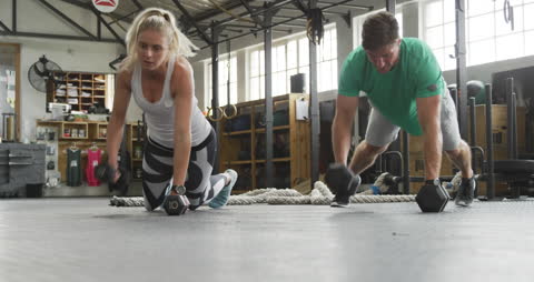 Athletic Man and Woman Performing Cross Training with Dumbbells in Gym