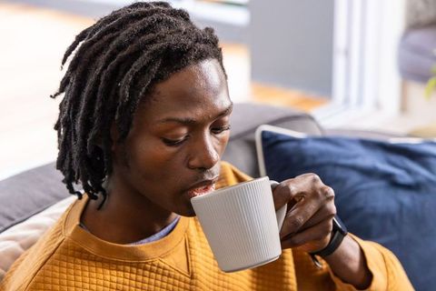 African american man sipping coffee on couch in cozy sunlit living room