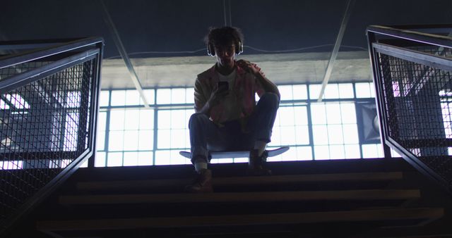 Young Man with Headphones Sitting on Skateboard in Urban Building - Download Free Stock Images Pikwizard.com