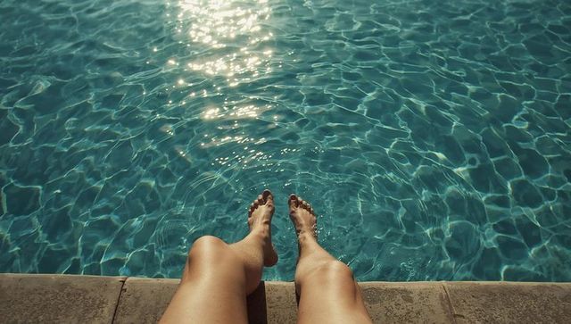 Sunlit legs dangling over turquoise pool water with painted nails, relaxing vacation