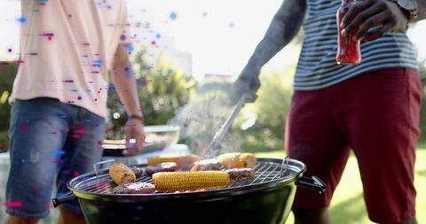 Backyard barbecue grilling corn and burgers with friends flipping burgers holding drink
