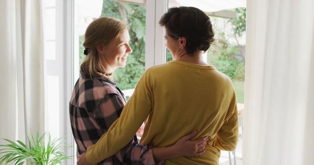 Caucasian lesbian couple hugging each other near the window at home. lgbt relationship and lifestyle concept