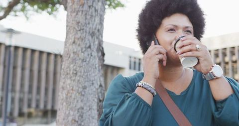 Smiling Plus Size Woman on Smartphone Holding Coffee Outdoors