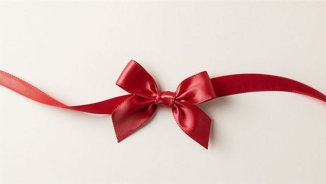 Scarlet satin bow with flowing ribbon tails on ivory surface for gift wrapping