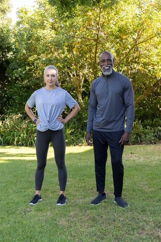 Mature couple exercising in sunlit backyard wearing athletic clothing and smartwatches
