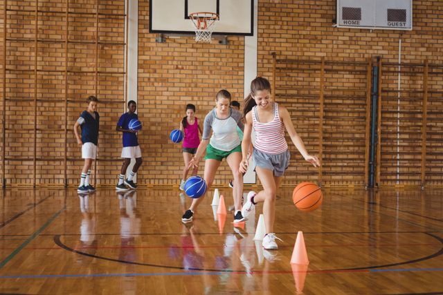 Group of high school kids practicing basketball dribbling drill using cones in a gym. Ideal for illustrating youth sports, teamwork, physical education, and fitness activities in educational or sports-related content.