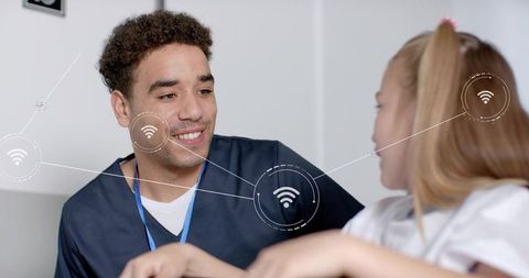 Smiling clinician in navy scrubs chatting with child, wireless icons indicating telehealth connectio